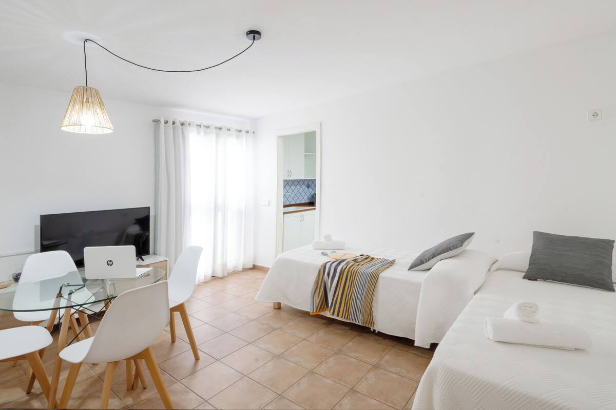 A modern hotel room with a dining area, a TV, and a bed with pillows.