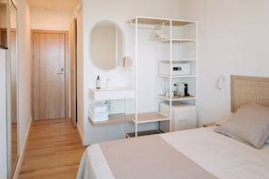 A hotel room with a bed, a wardrobe, a vanity with a mirror, a shelf with toiletries, and a bedside table. - Hotel Rosamar (Formentera)