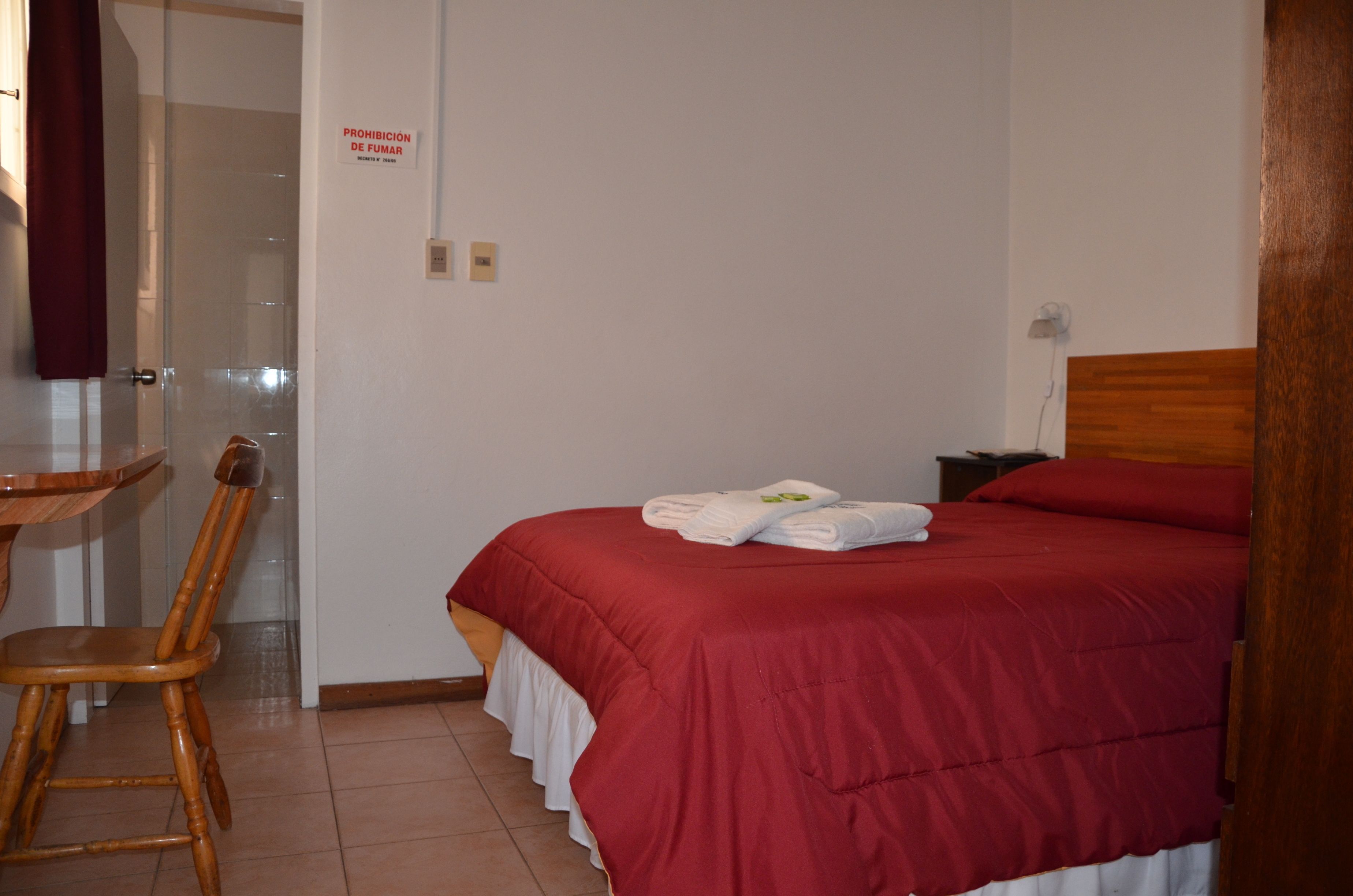 Een hotelkamer met een bed, een houten stoel, een tafeltje en een bordje aan de muur.