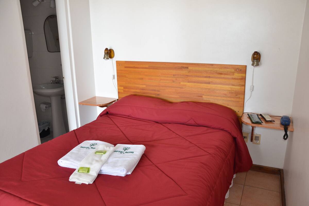 A hotel room with a wooden headboard, a red bedspread, and two towels with the hotel logo.
