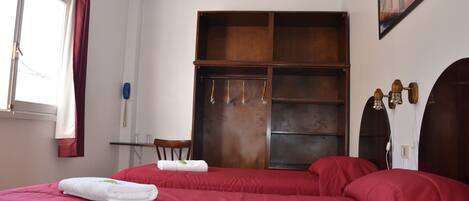 A hotel room with two beds, a wooden wardrobe, a desk, and a chair.