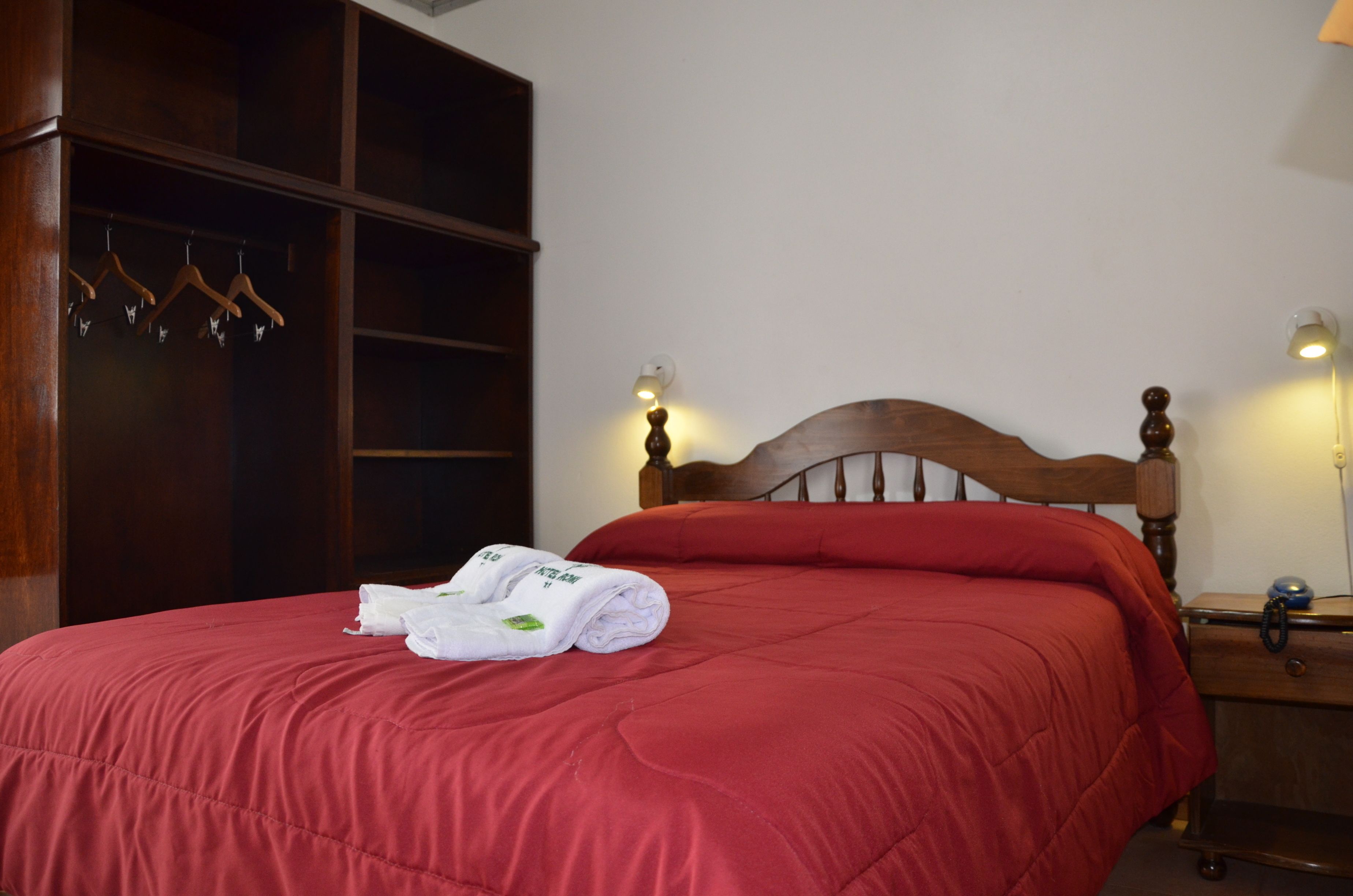 A neatly made bed with a red bedspread, a wooden headboard, and a set of white towels on the bed.