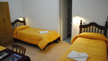 Una habitación con dos camas, un armario de madera, una mesa con una revista y una puerta que da a otra estancia.