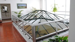 A conservatory with a glass roof, surrounded by potted plants and a painting on the wall. - Hotel Romi (Colonia del Sacramento)