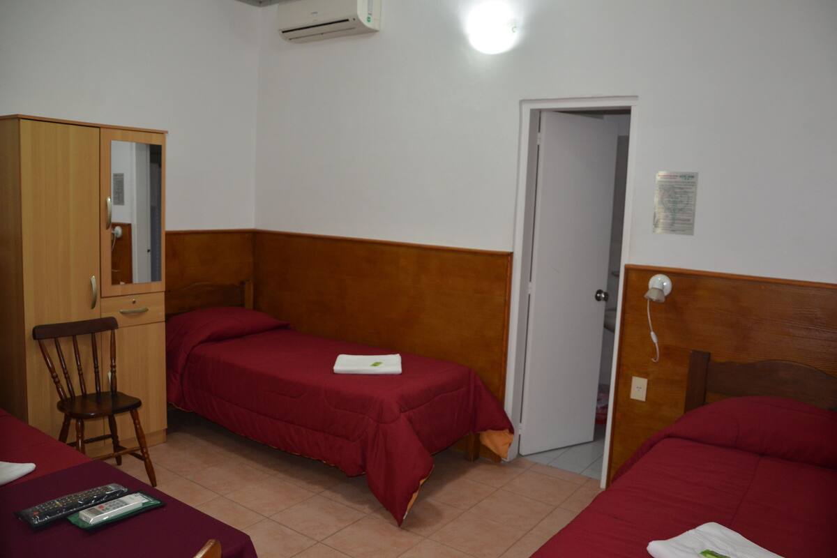 A room with two single beds, a wooden wardrobe, a desk with a chair, and a door leading to another room.