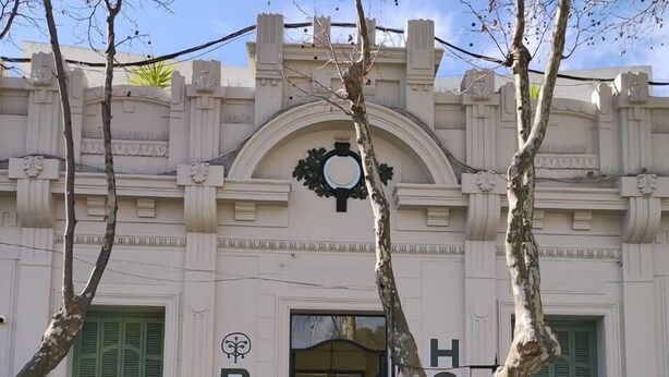 A building with a classic architectural style, featuring a prominent arched entrance and decorative moldings. The name "ROMI" is displayed above the entrance. - Hotel Romi (Colonia del Sacramento)