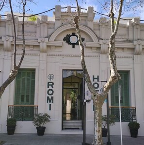 A building with a classic architectural style, featuring a prominent arched entrance and decorative moldings. The name "ROMI" is displayed above the entrance. - Hotel Romi (Colonia del Sacramento)