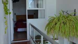 A staircase with a railing, a bed with a red blanket, and a fern plant. - Hotel Romi (Colonia del Sacramento)