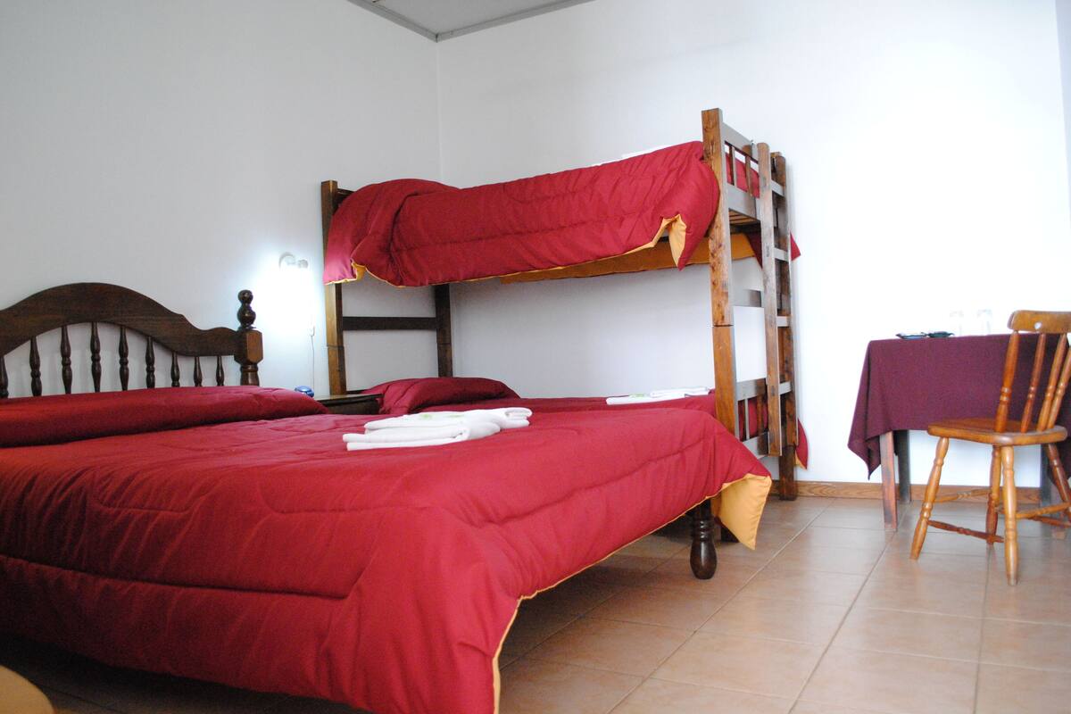 A bunk bed with red bedding, a wooden chair, and a table with a purple tablecloth.
