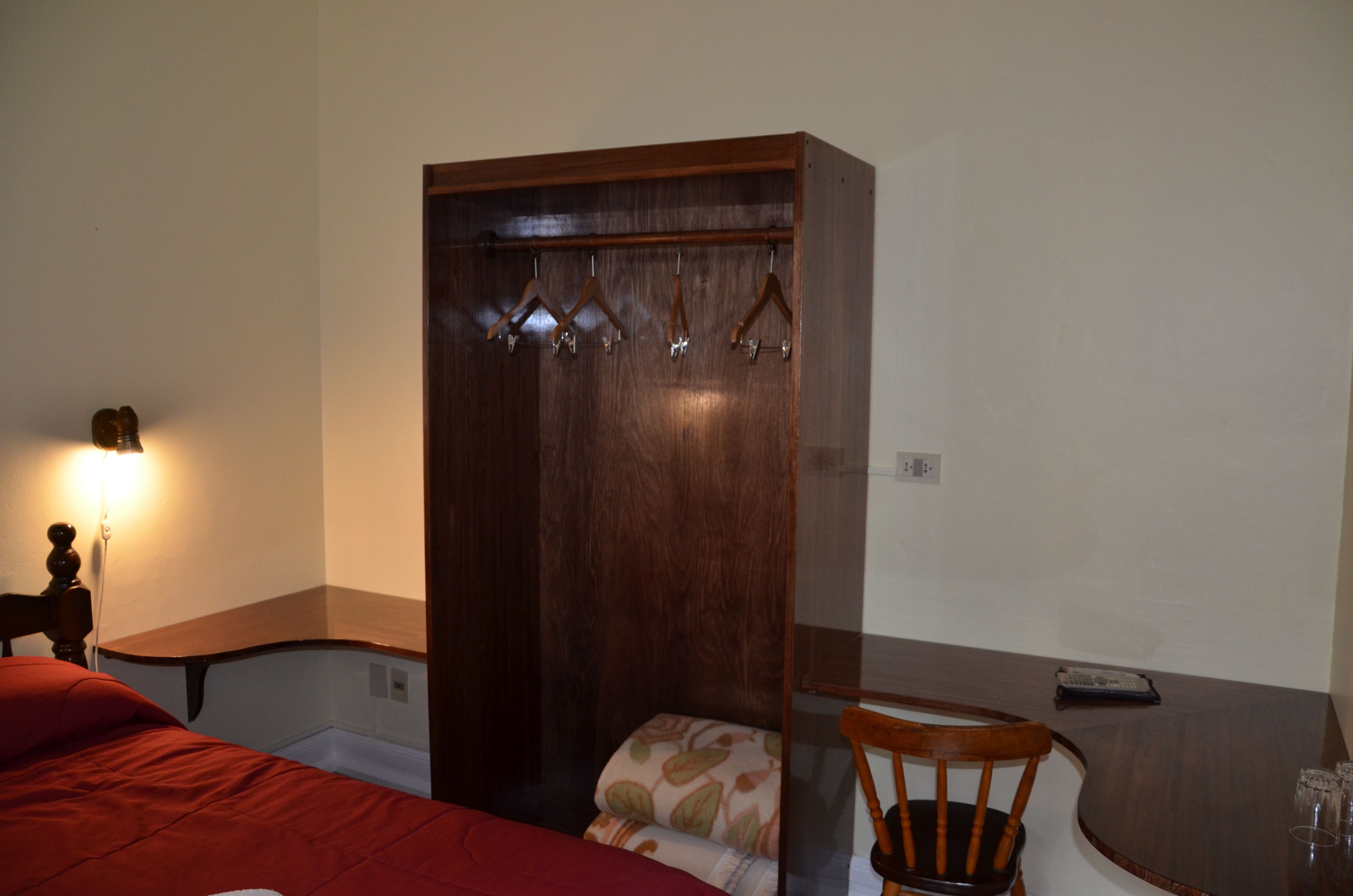 Une chambre à coucher comprenant un lit, une armoire en bois, une chaise, une table et un luminaire fixé au mur.