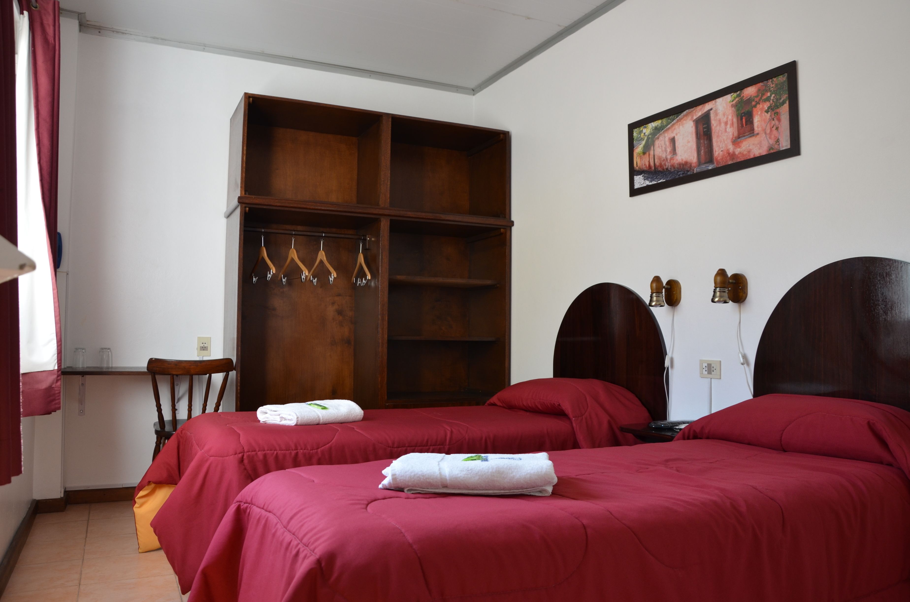 Habitación de hotel con dos camas, un armario de madera, un escritorio y un cuadro en la pared.