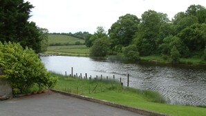 A riverside view with a grassy area and a paved path leading to a dock. - Corrigans Shore House (Enniskillen)