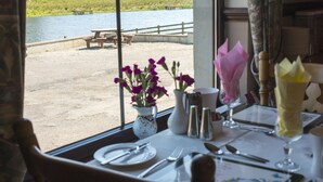 A dining table with a view of a lake and grassy area outside. - Corrigans Shore House (Enniskillen)