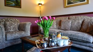 A living room with a floral sofa, a coffee table with a vase of tulips, and a tray with pastries and a teapot. - Corrigans Shore House (Enniskillen)