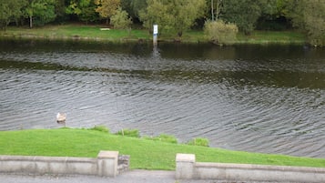 Ein Fluss mit einer grasbewachsenen Uferböschung und einer Betonmauer.
