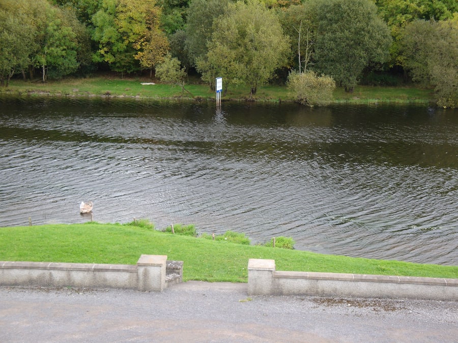 Ein Fluss mit einer grasbewachsenen Uferböschung und einer Betonmauer.
