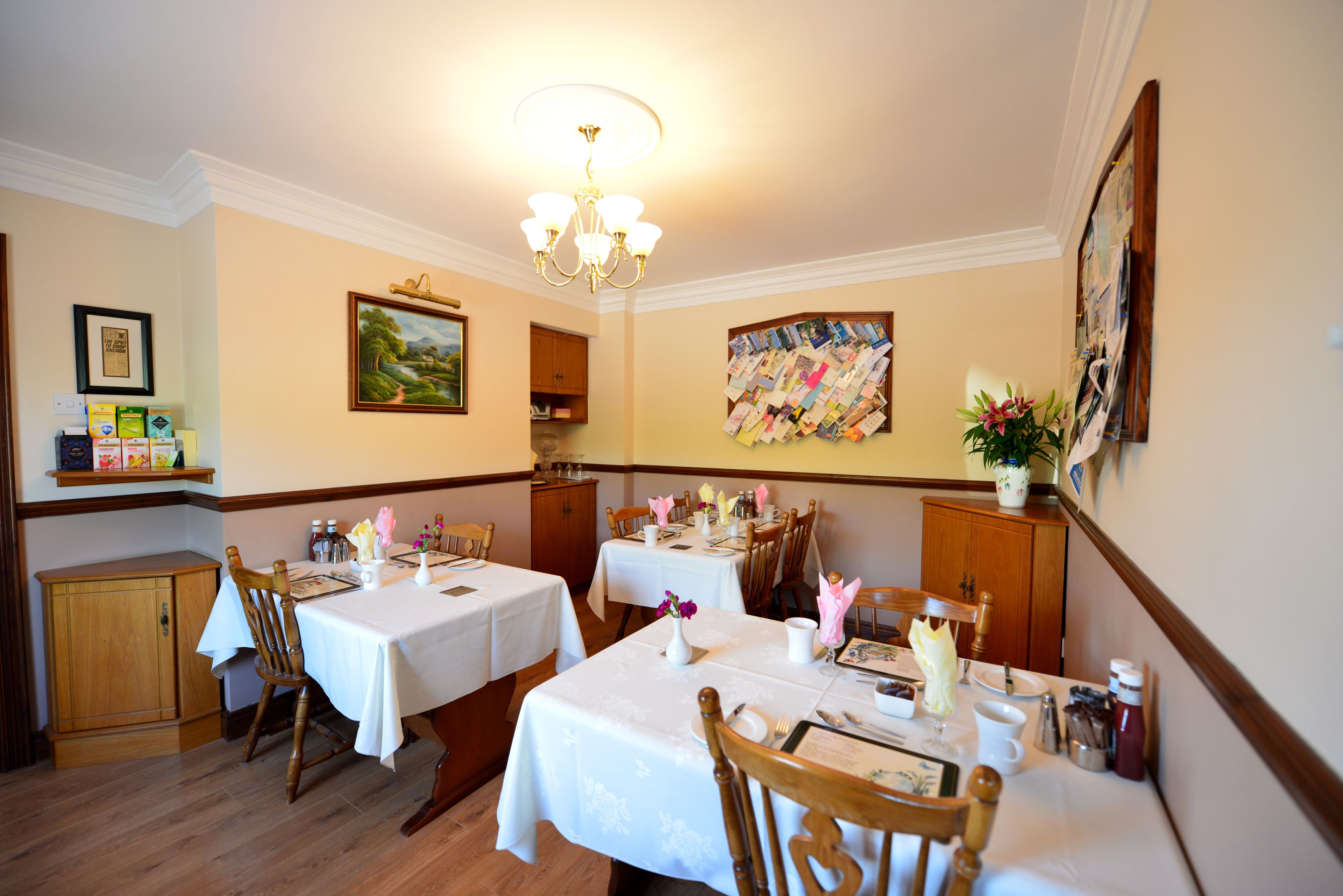 A dining area with two tables set for four, wooden chairs, a chandelier, and wall art.