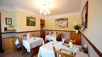 A dining area with two tables set for four, wooden chairs, a chandelier, and wall art.