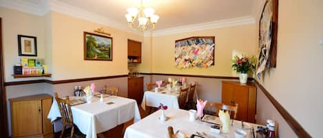 A dining area with two tables set for four, wooden chairs, a chandelier, and wall art.