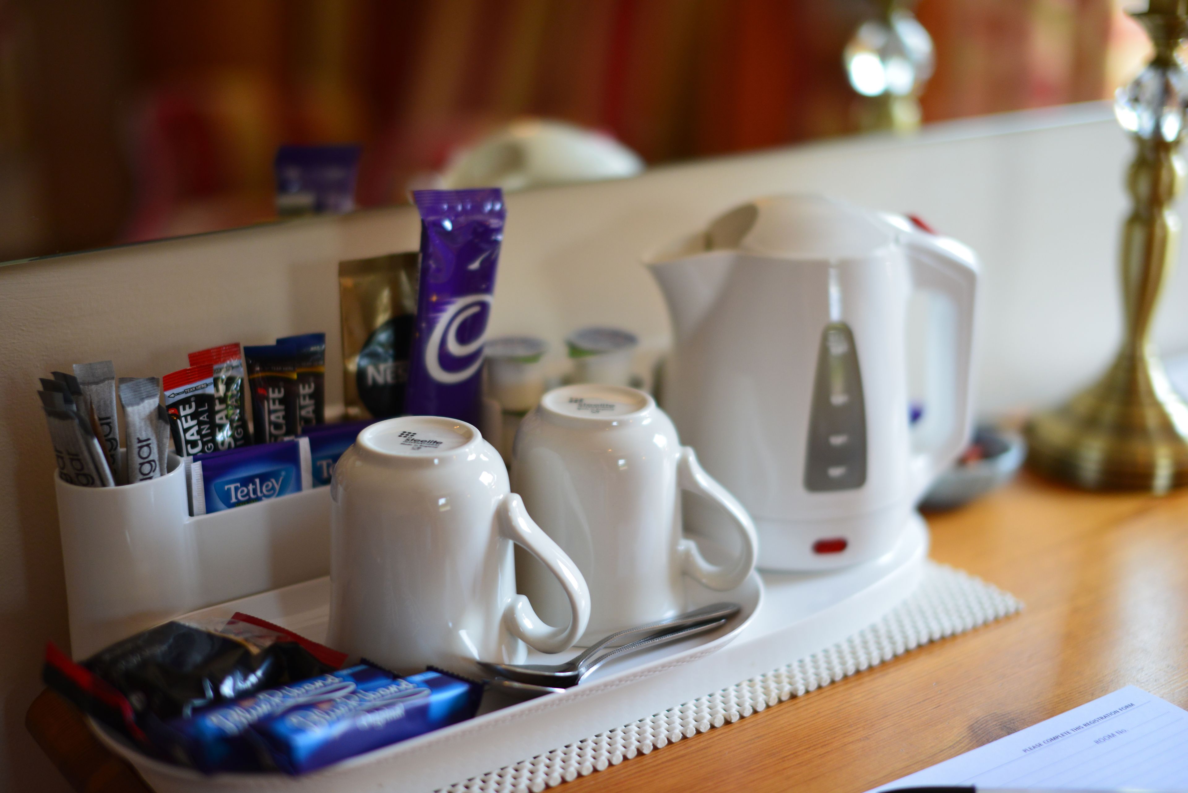 A hotel room's breakfast setup with a coffee maker, two white mugs, a tray with coffee packets, and a spoon.