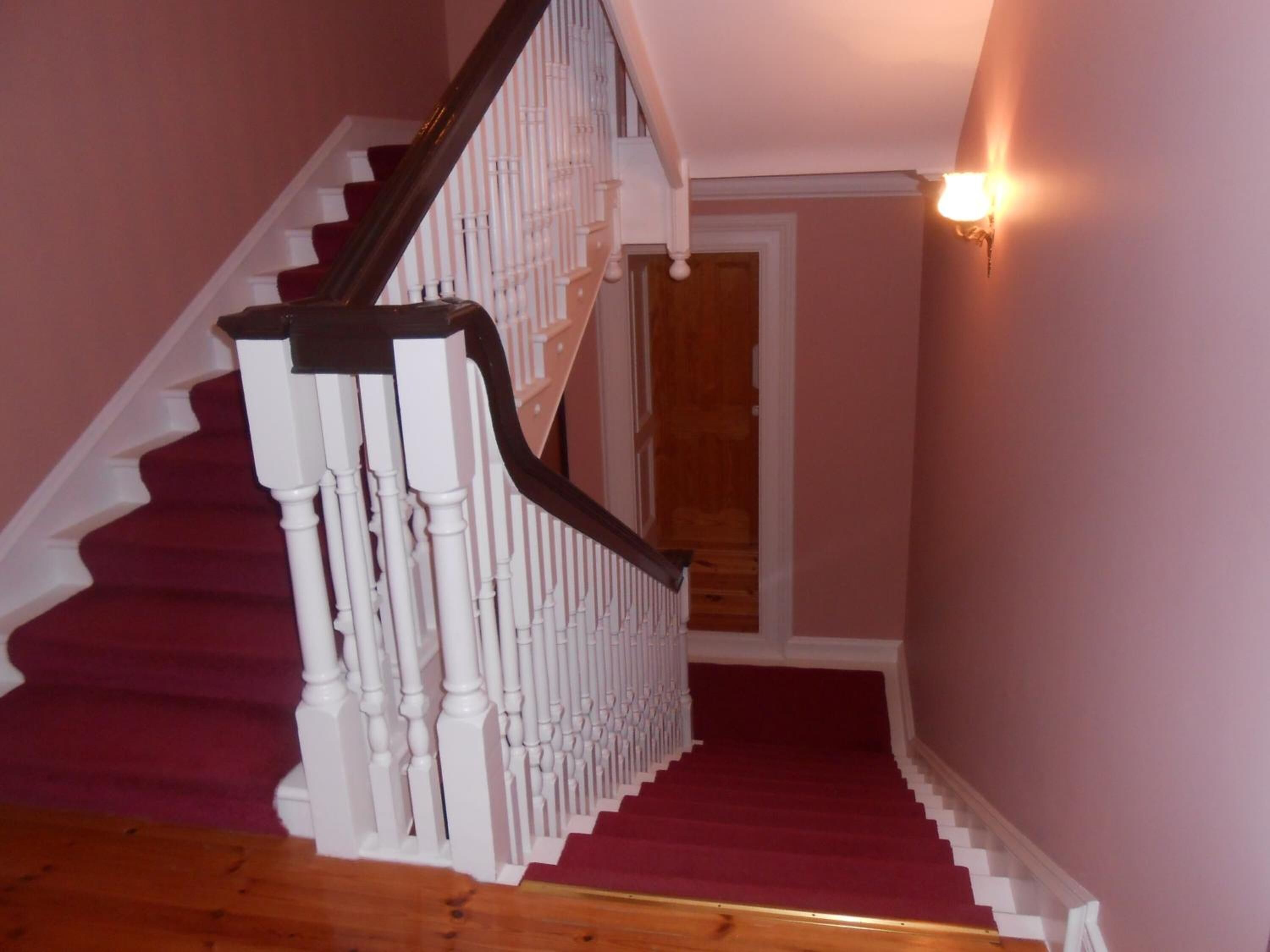 A staircase with white balusters and red carpeted steps leading to a door.