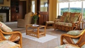 A cozy living room with wicker furniture, a wooden coffee table, and a view of the countryside through large windows. - The Arches (Arvagh)