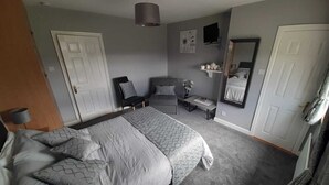 A bedroom with a large bed, a chair, a small table, a mirror, and a door. - The Arches (Arvagh)