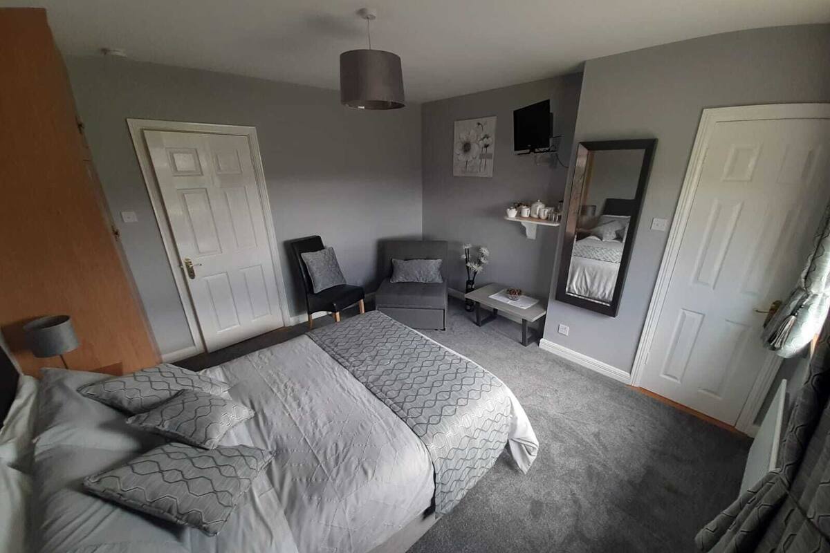 A bedroom with a large bed, a chair, a small table, a mirror, and a door.