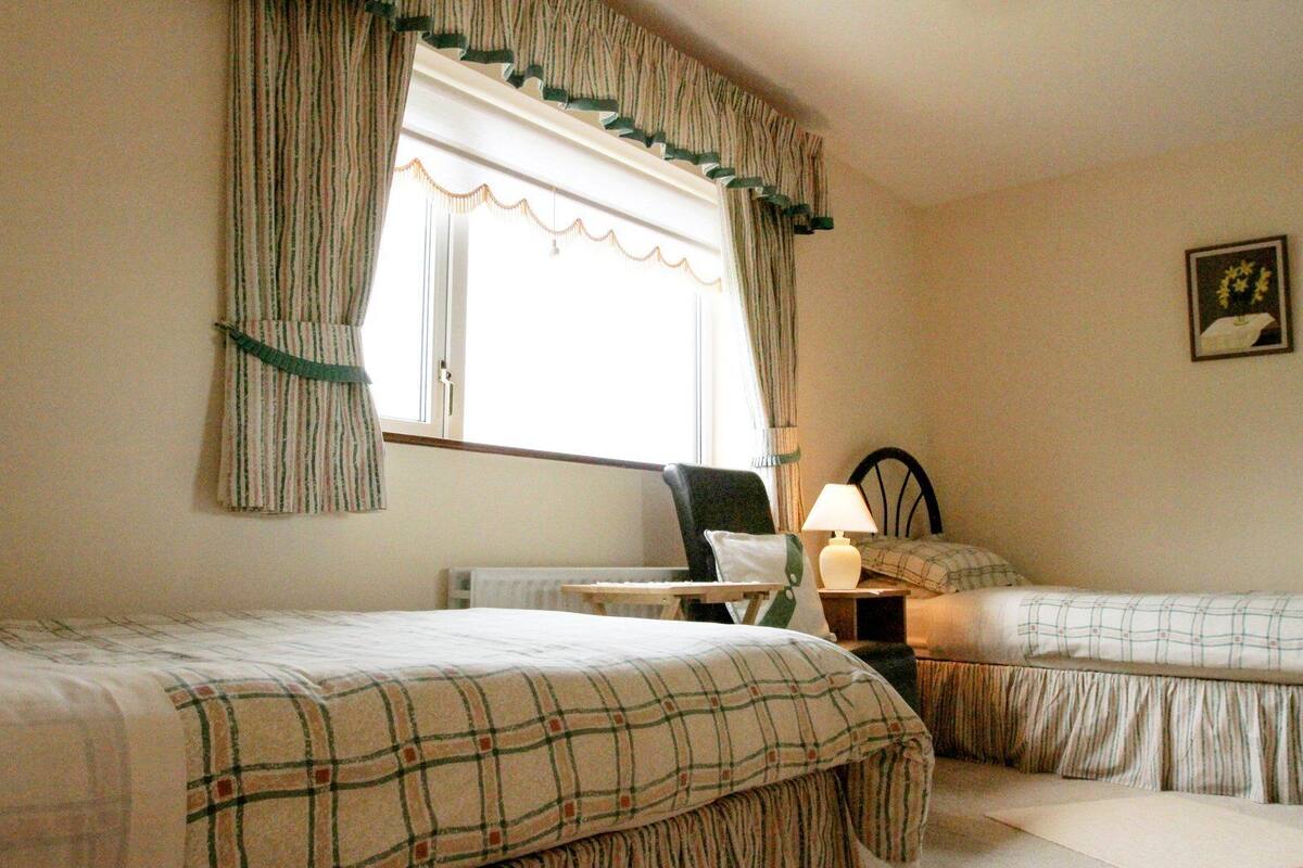 A hotel room with two beds, a nightstand, a lamp, and a window with curtains.