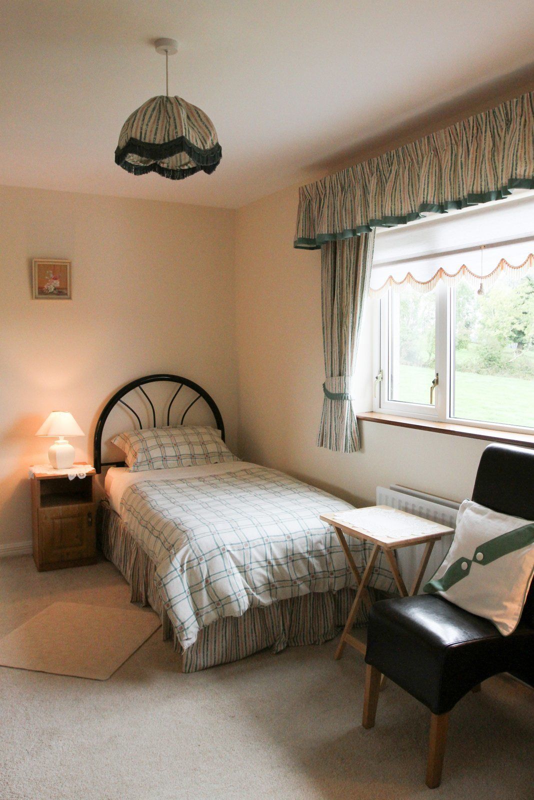 A bedroom with a bed, bedside table, lamp, chair, and a window with curtains.
