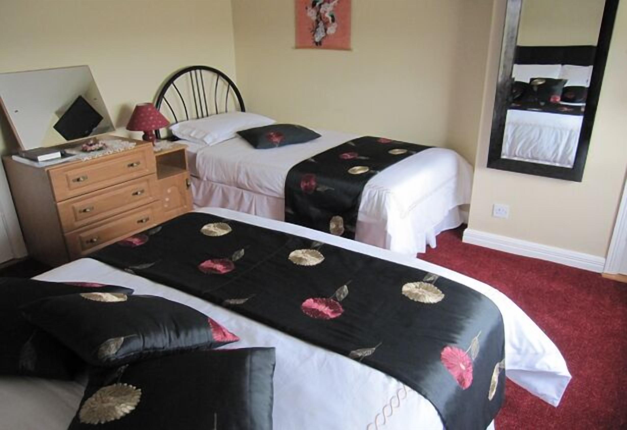 A hotel room with two beds, a wooden dresser, a mirror, and a red carpet.