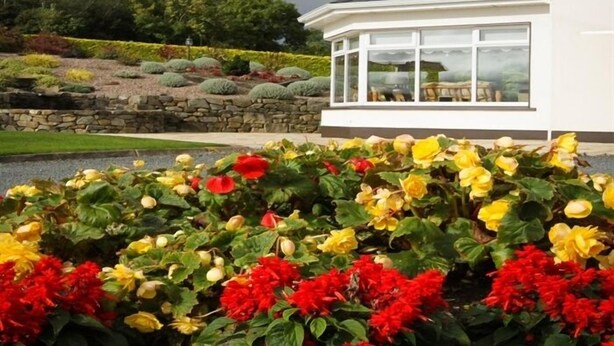 A modern house with a conservatory, surrounded by a well-maintained garden with colorful flowers. - The Arches (Arvagh)
