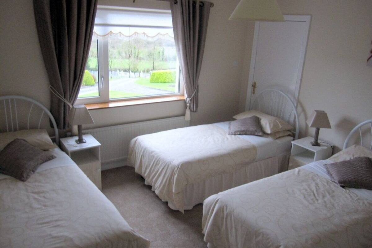 A bedroom with two single beds, a window with curtains, a radiator, and a lamp on a bedside table.