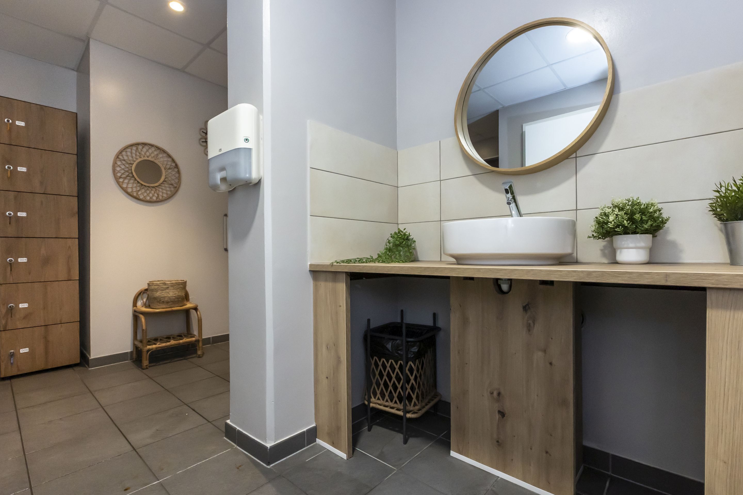 A bathroom with a wooden vanity, a round mirror, a sink, and a small potted plant.
