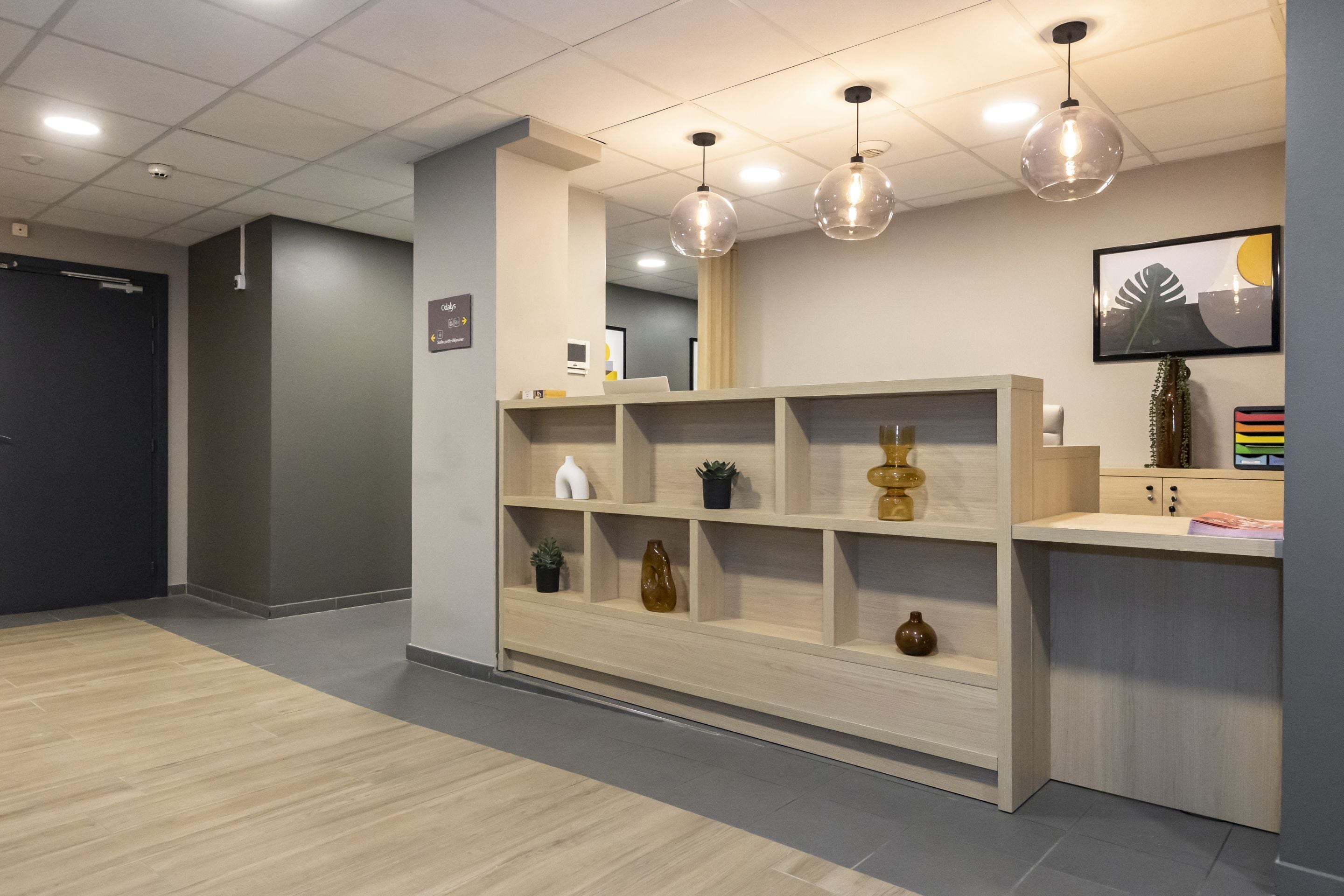 Zona de recepción con mostrador de madera, estanterías decorativas e iluminación colgante.