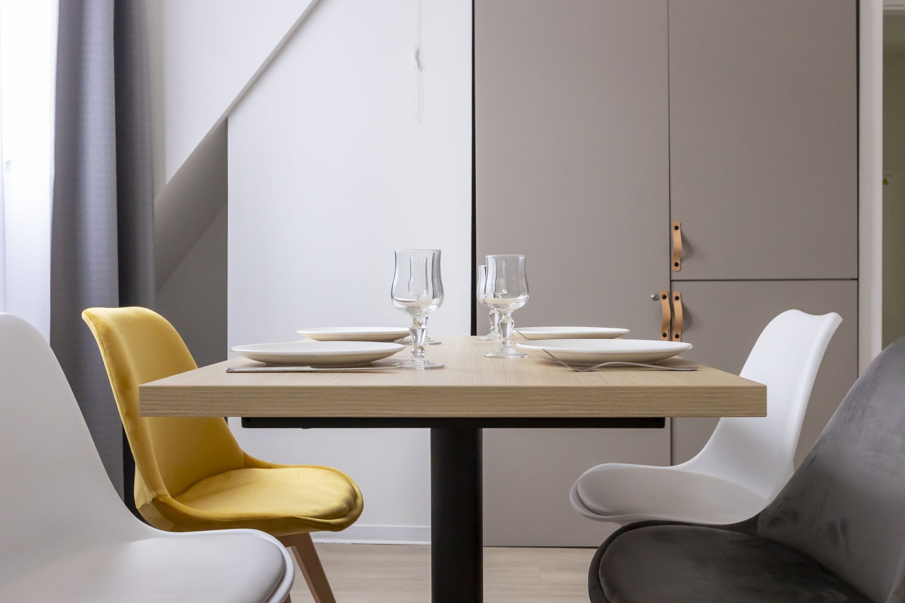 A dining area with a wooden table set for two, surrounded by modern chairs in white, yellow, and gray.