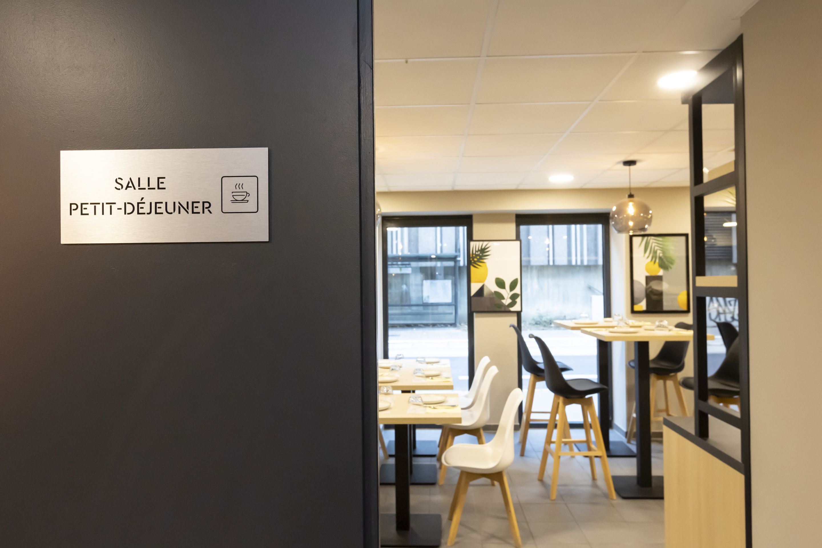 A modern dining area with a sign reading "SALLE PETIT-DÉJEUNER" and tables set for dining.