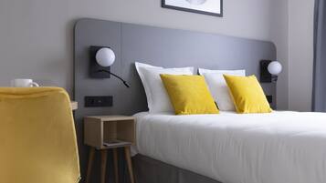 A modern hotel room with a bed, two bedside lamps, a small wooden nightstand, a yellow chair, and a framed picture on the wall.