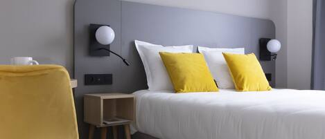 A modern hotel room with a bed, two bedside lamps, a small wooden nightstand, a yellow chair, and a framed picture on the wall.