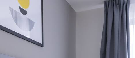 Une chambre d’hôtel avec un lit, deux oreillers, une lampe fixée au mur et une fenêtre avec des rideaux.