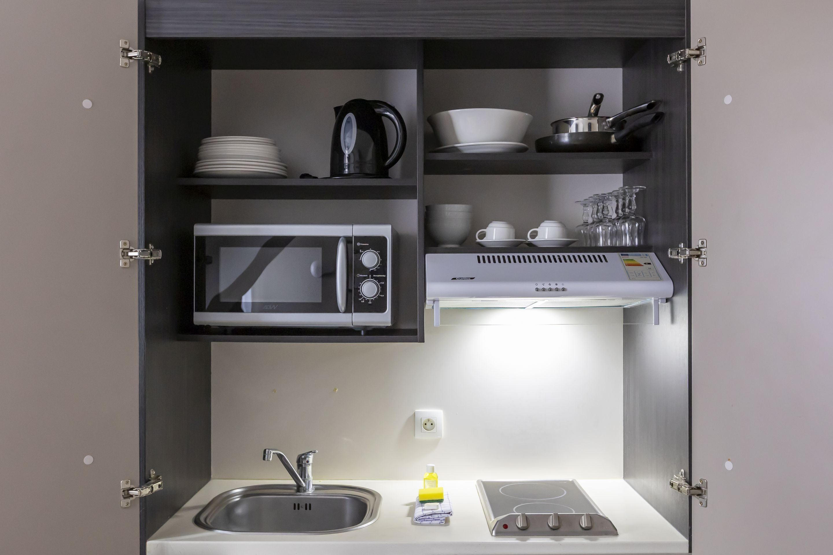 Una cocina compacta con microondas, hervidor y placa de inducción.