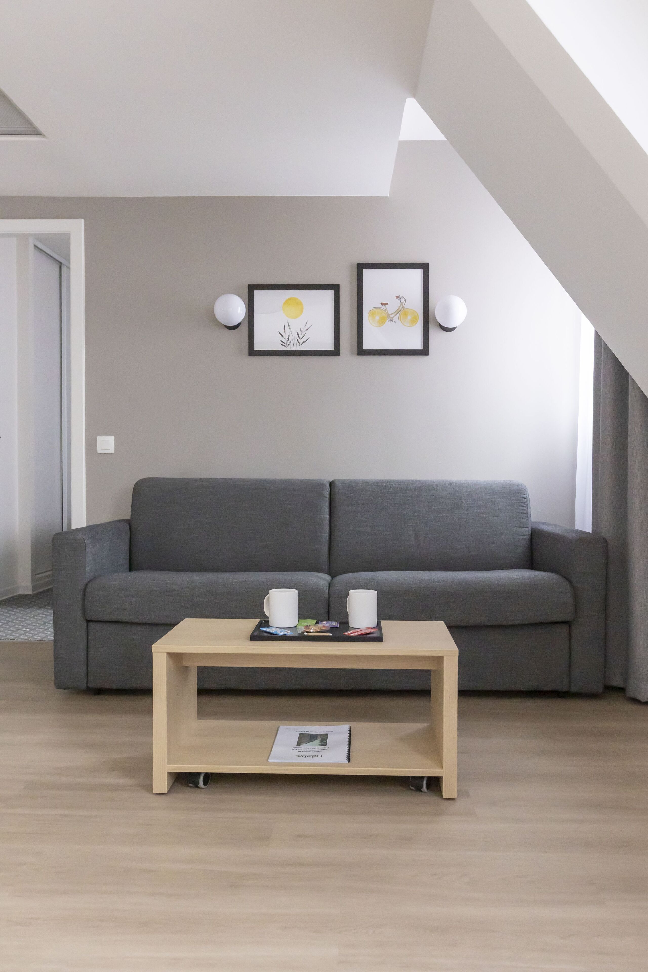 A modern living room with a grey sofa, a wooden coffee table, and two framed pictures on the wall.