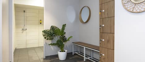 A bathroom with a shower, a potted plant, a bench, and a wooden cabinet with a mirror.