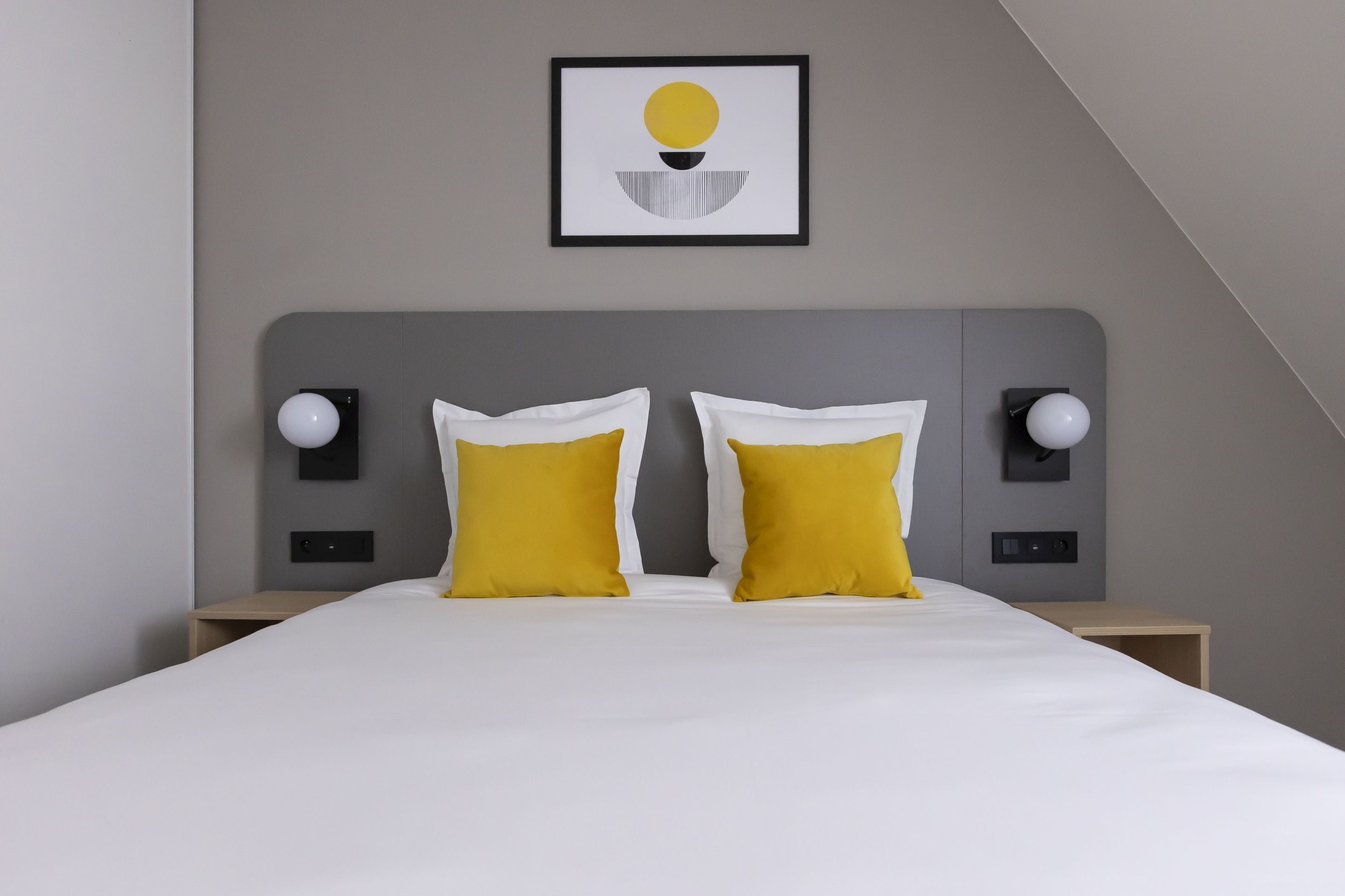 A modern hotel room with a large bed, two bedside tables, and a framed artwork on the wall.