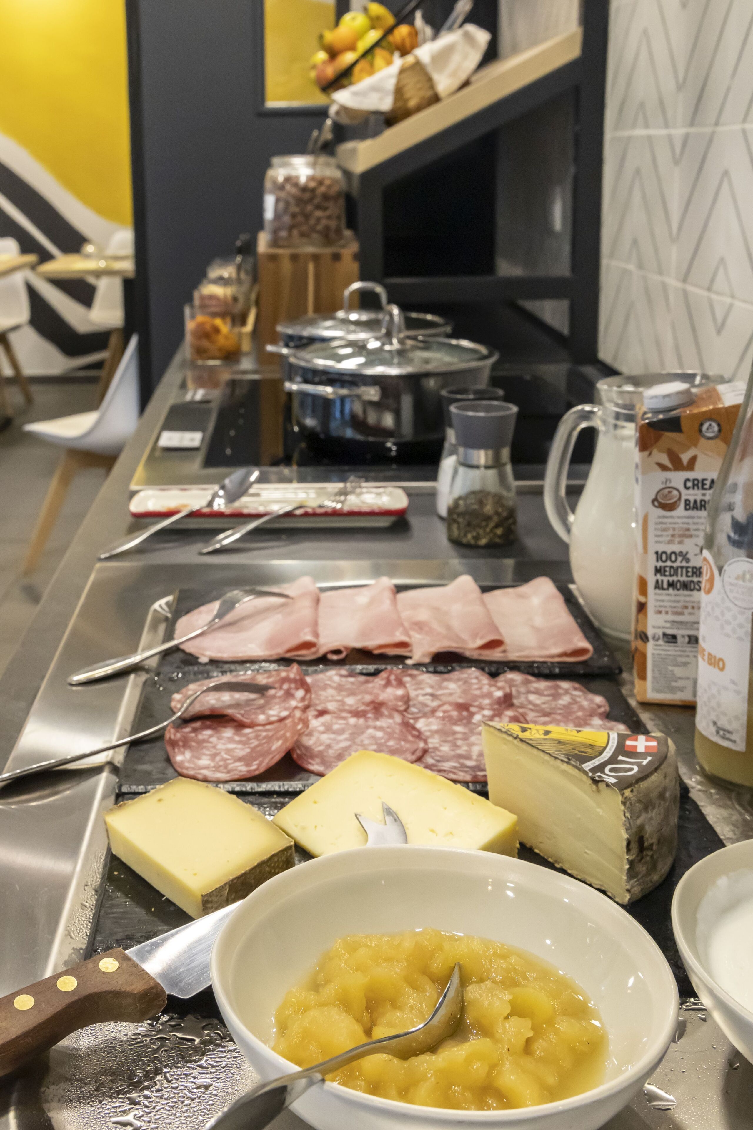A buffet table with various cheeses, meats, and a bowl of fruit salad.