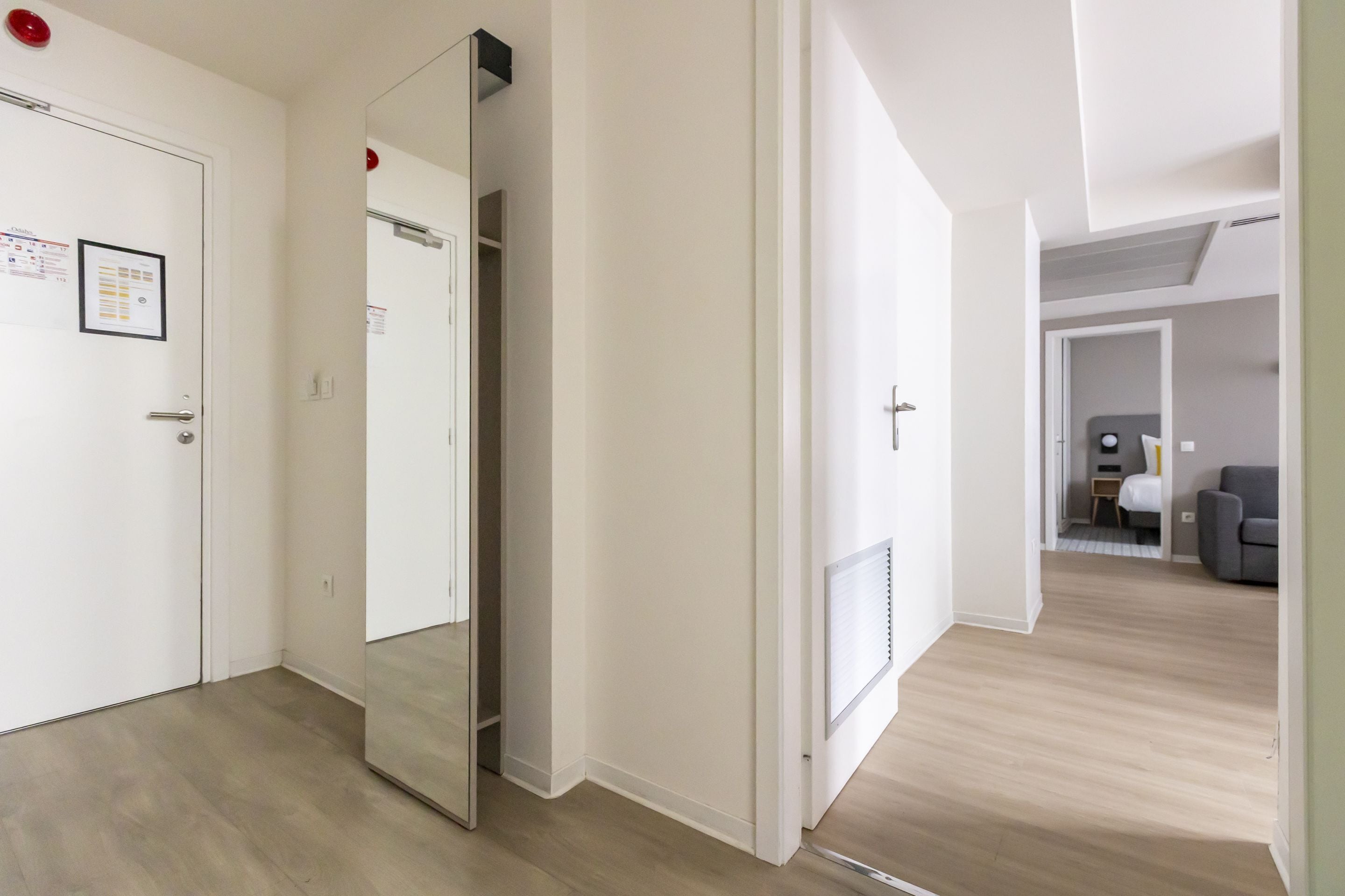 Un couloir avec une porte de placard à miroir, un radiateur et un aperçu d’une chambre à coucher avec un lit et une table de chevet.