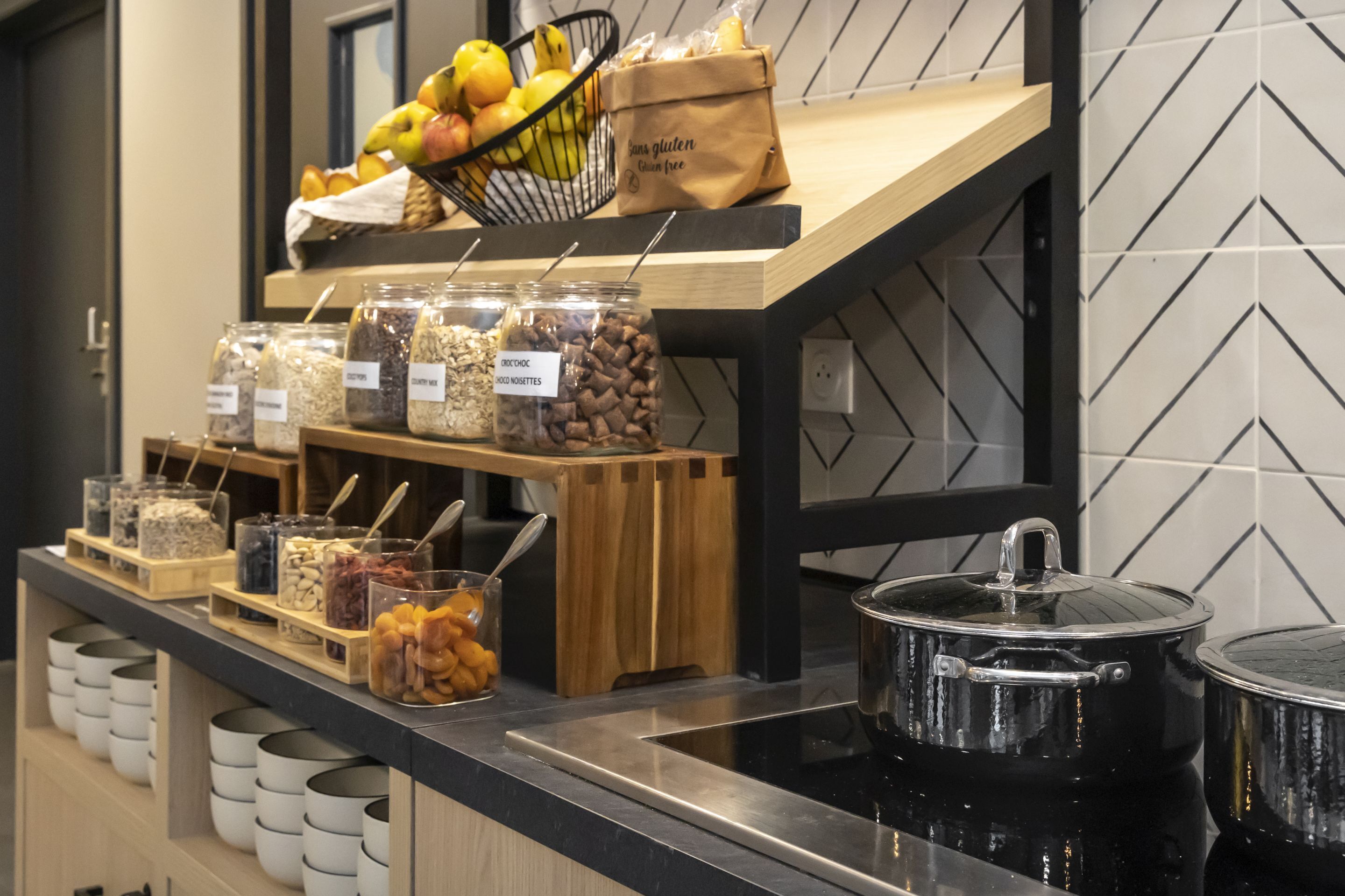 A buffet setup with various food items, including fruits, nuts, and grains, displayed on a counter with a black countertop and wooden shelves.