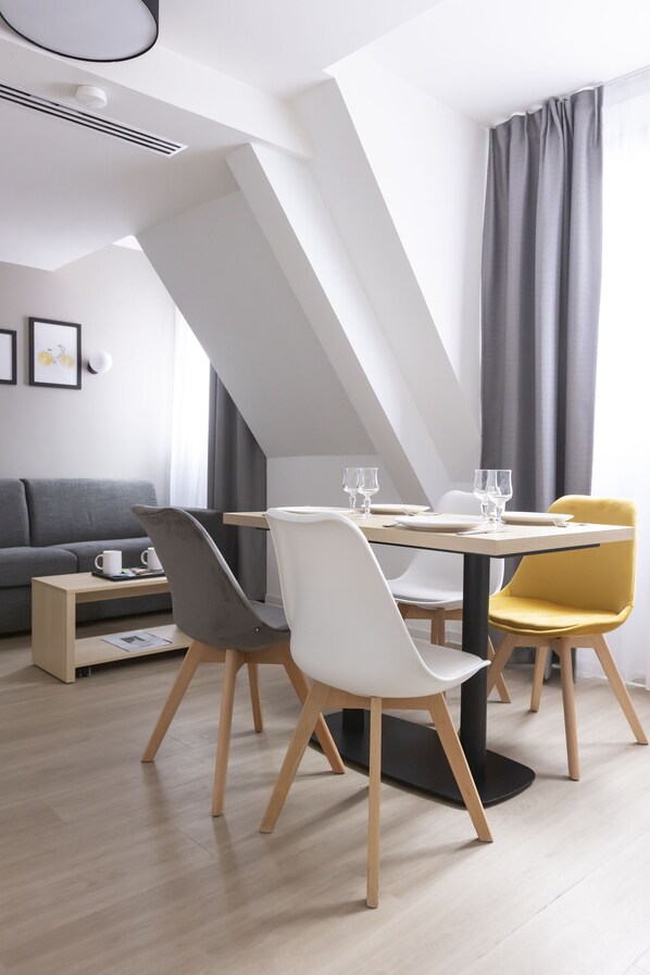 Un comedor moderno con una mesa lista para dos personas, un sofá y una mesita de centro en un espacio amplio y luminoso con techo inclinado.