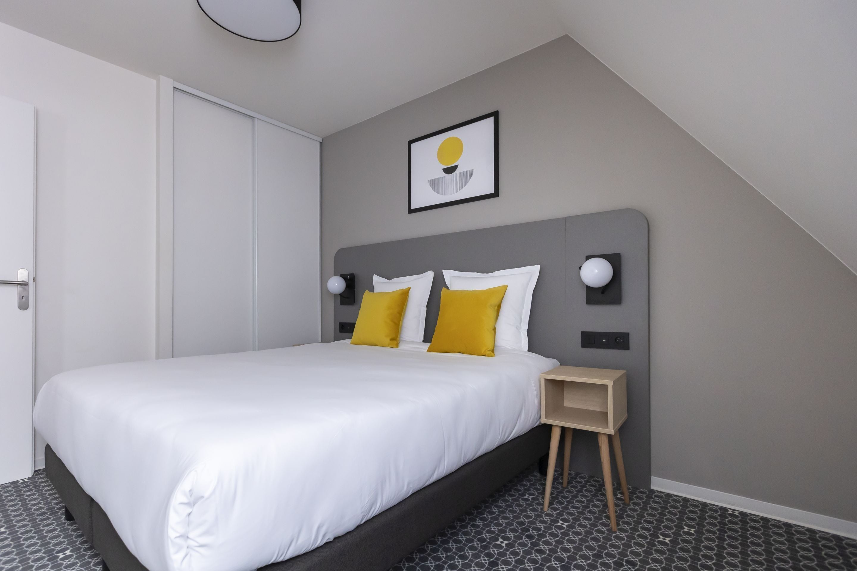 A modern bedroom with a large bed, a bedside table, and a wall-mounted light fixture.