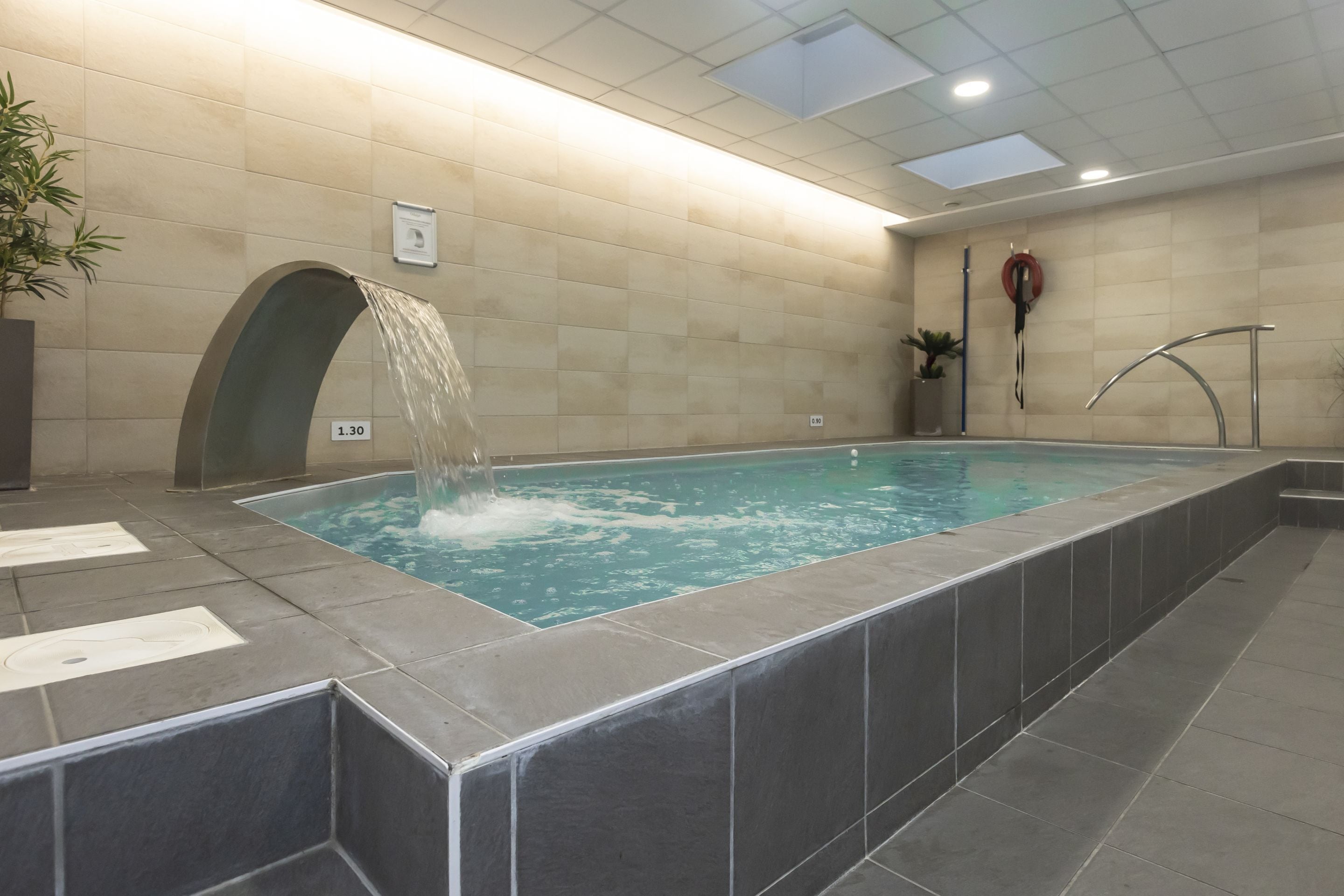 A swimming pool with a water feature, tiled walls, and a lifebuoy on the wall.